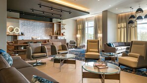 Un moderno vestíbulo de hotel con un sofá, sillones, una mesa de centro de vidrio y piso alfombrado.