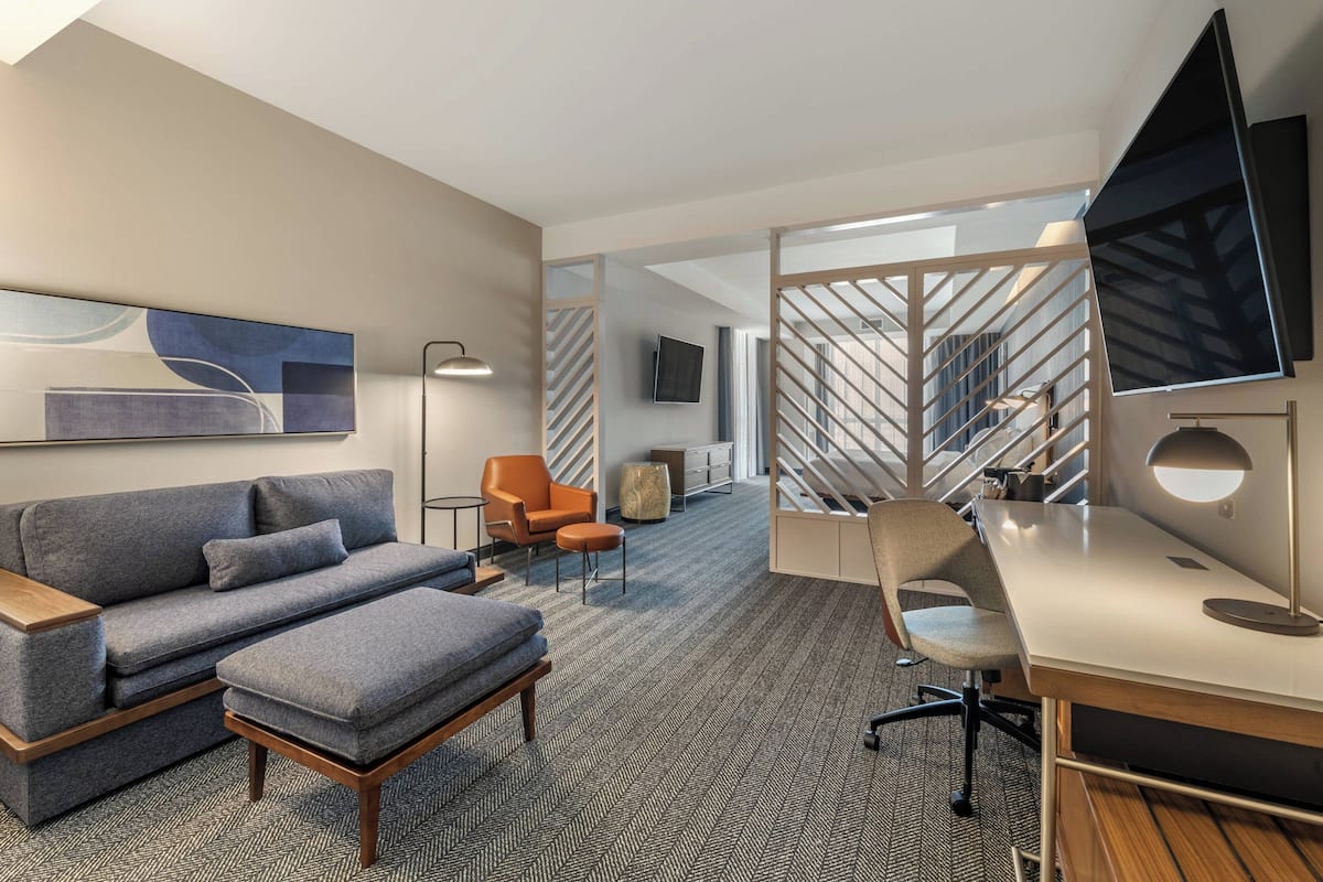 Une chambre d’hôtel moderne équipée d’un canapé, d’un pouf, d’un bureau, d’une chaise et d’un grand téléviseur.