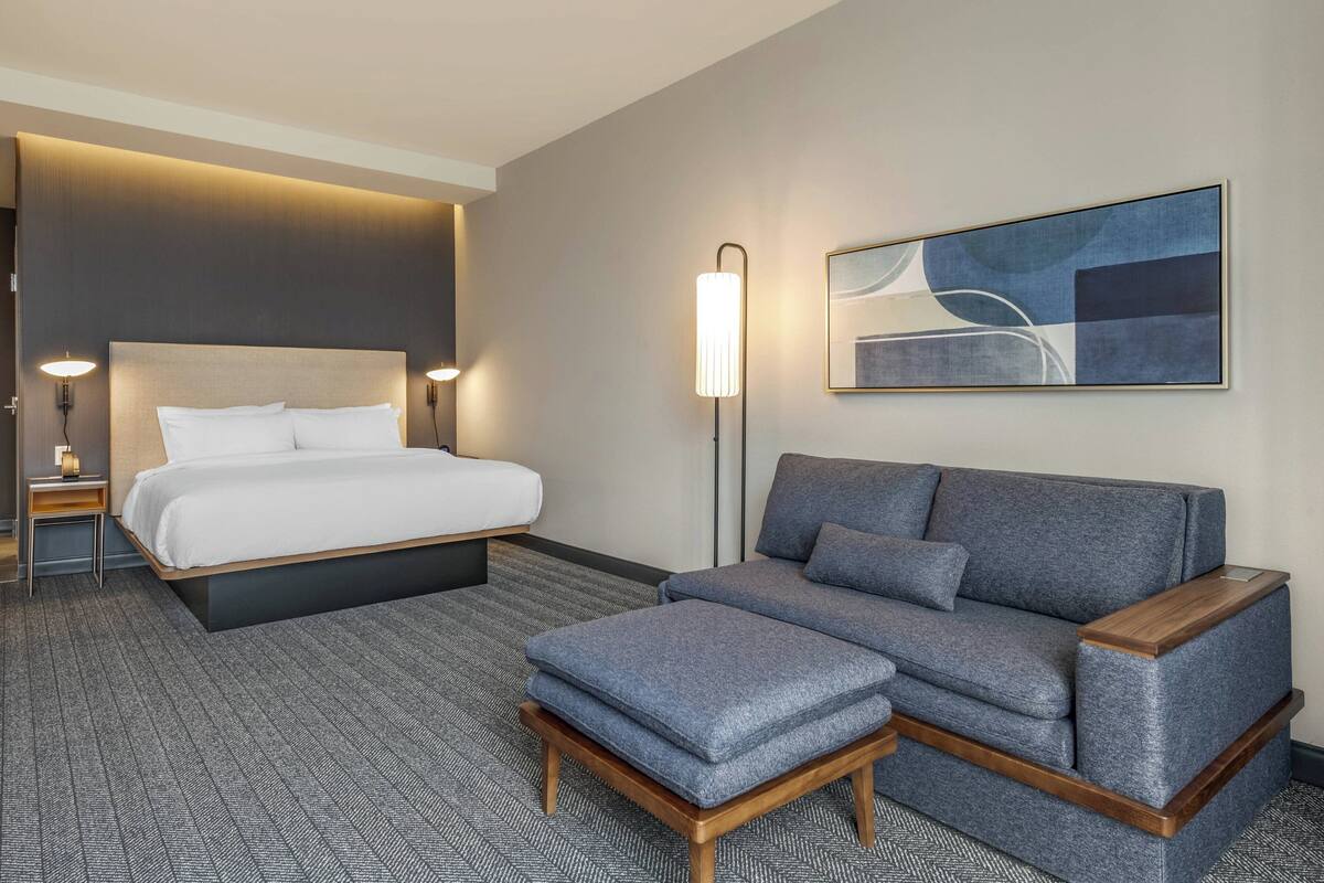 Une chambre d’hôtel avec un lit, un canapé, une petite table et une lampe sur pied.