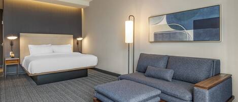 A hotel room with a bed, a sofa, a small table, and a floor lamp.