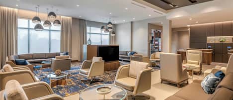 Un vestíbulo de hotel moderno con un amplio espacio de estar, un televisor de pantalla plana y una zona de bar.