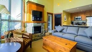 A modern living room with a stone fireplace, a grey sofa, and a wooden coffee table. - Incredible Views / Modern Updates / Hot Tub (Fernie)