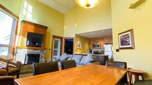 A dining area with a wooden table and chairs, a fireplace, and a kitchen in the background. - Incredible Views / Modern Updates / Hot Tub (Fernie)