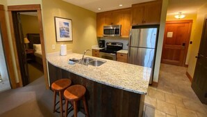 A kitchen with granite countertops, stainless steel appliances, wooden cabinets, and two bar stools. - Incredible Views / Modern Updates / Hot Tub (Fernie)