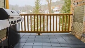 Ein Balkon mit Grill, gefliestem Boden und Blick auf Bäume und ein Gebäude.