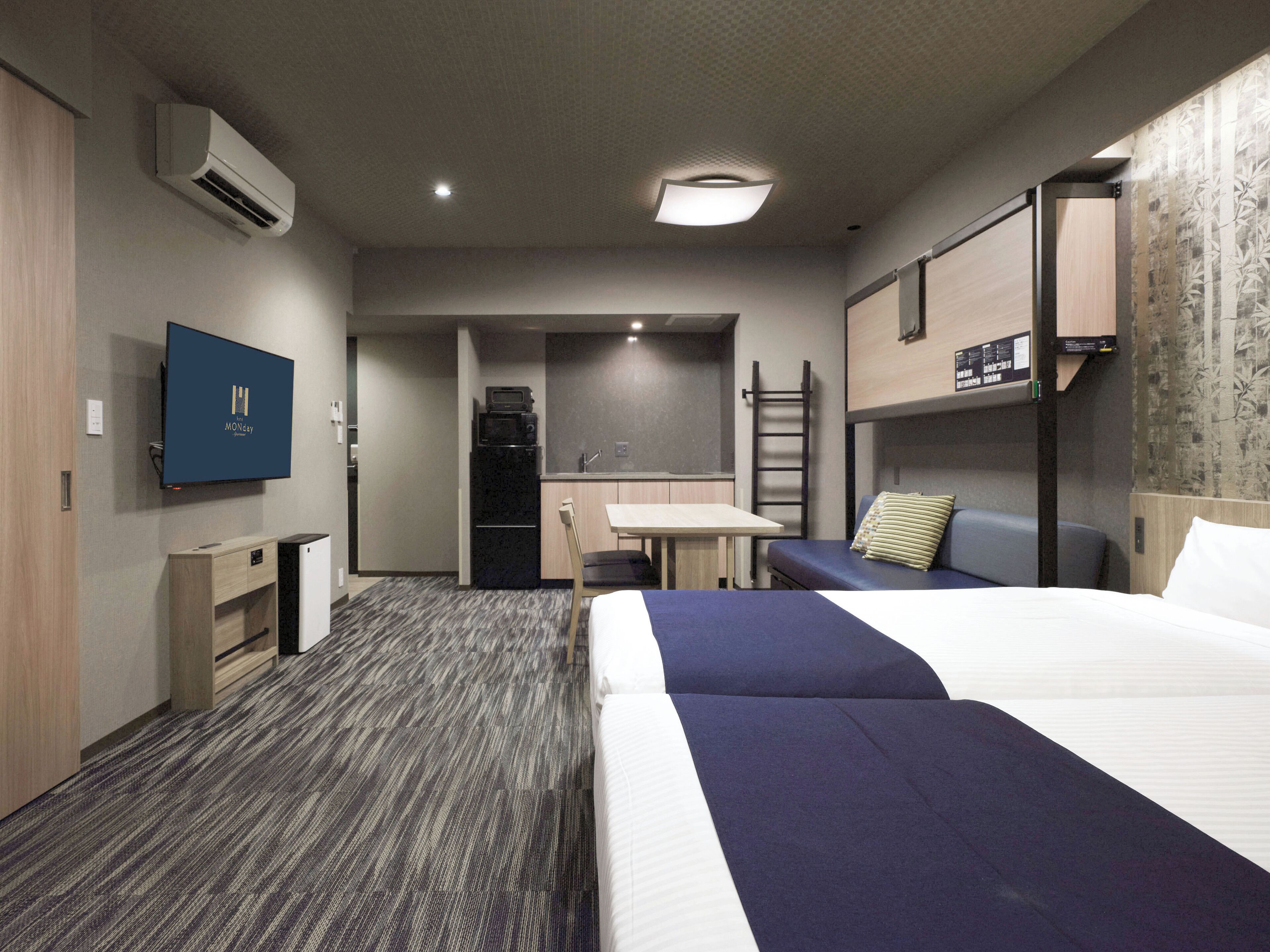 Una habitación de hotel con cama, escritorio, microondas, televisor y literas.