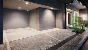 A modern building exterior with a paved entrance area, recessed lighting, and a small landscaped section with a tree. - MONday Apart Premium Akihabara (Tokyo)