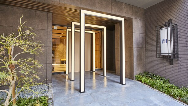 A modern building entrance with a metal frame structure, a stone wall, and a small tree. - MONday Apart Premium Akihabara (Tokyo)