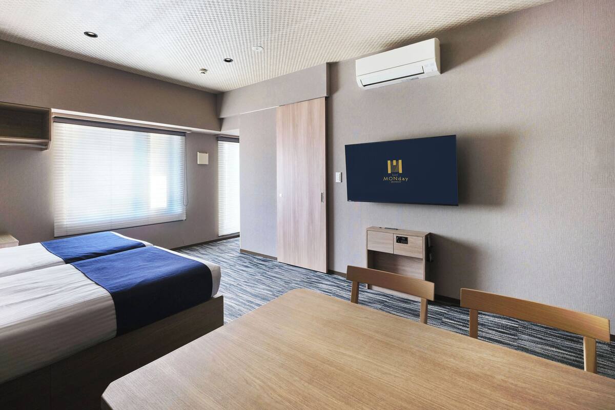 Ein Hotelzimmer mit Bett, Schreibtisch, Stuhl, Fernseher und Klimaanlage.
