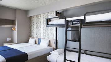 A hotel room with two single beds, a bunk bed, a wardrobe, and a small shelf.