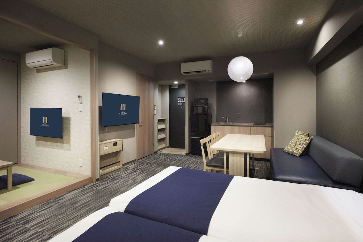 Ein Hotelzimmer mit Bett, Schreibtisch, Sofa, Fernseher und einer Küchenzeile.
