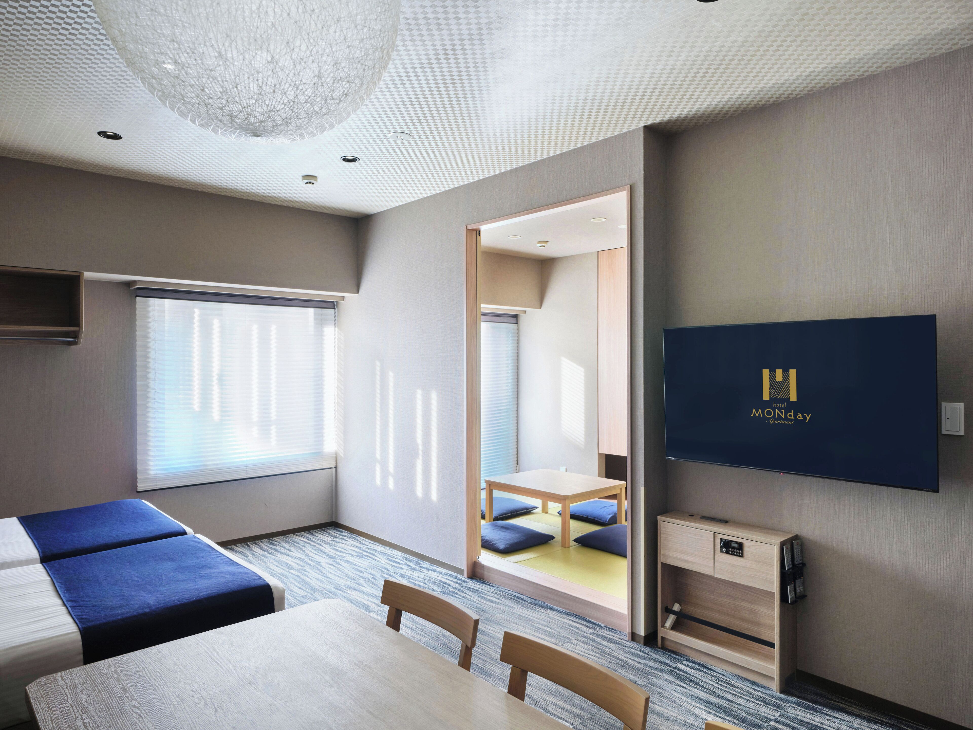 A hotel room with a bed, a desk, a chair, a TV, and a view of the outside.