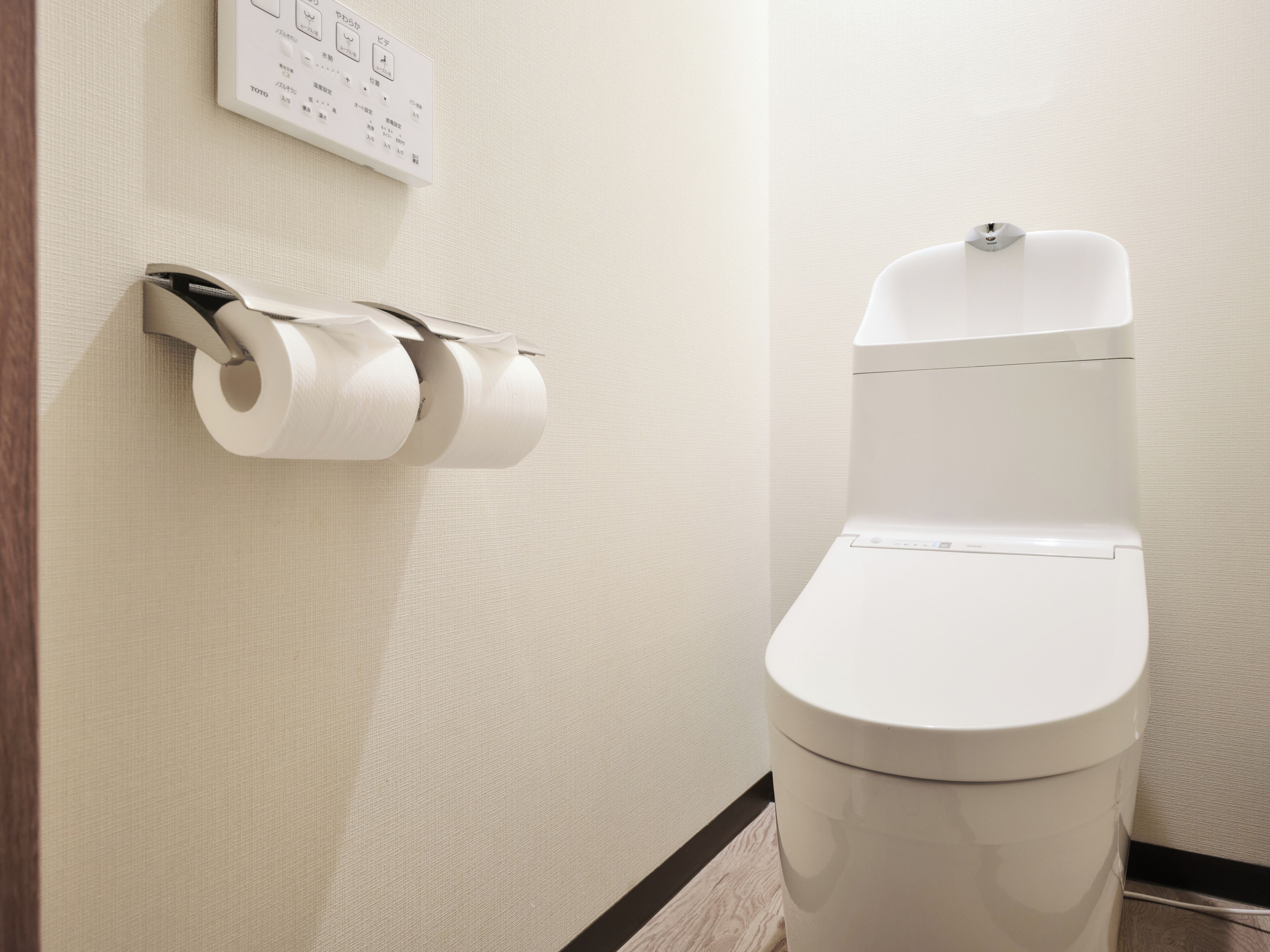 A toilet with a white lid and a flush handle, a toilet paper holder with two rolls, and a control panel with Japanese text.