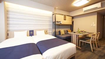 Habitación de hotel con dos camas, un sofá, una mesita con sillas y una kitchenette.