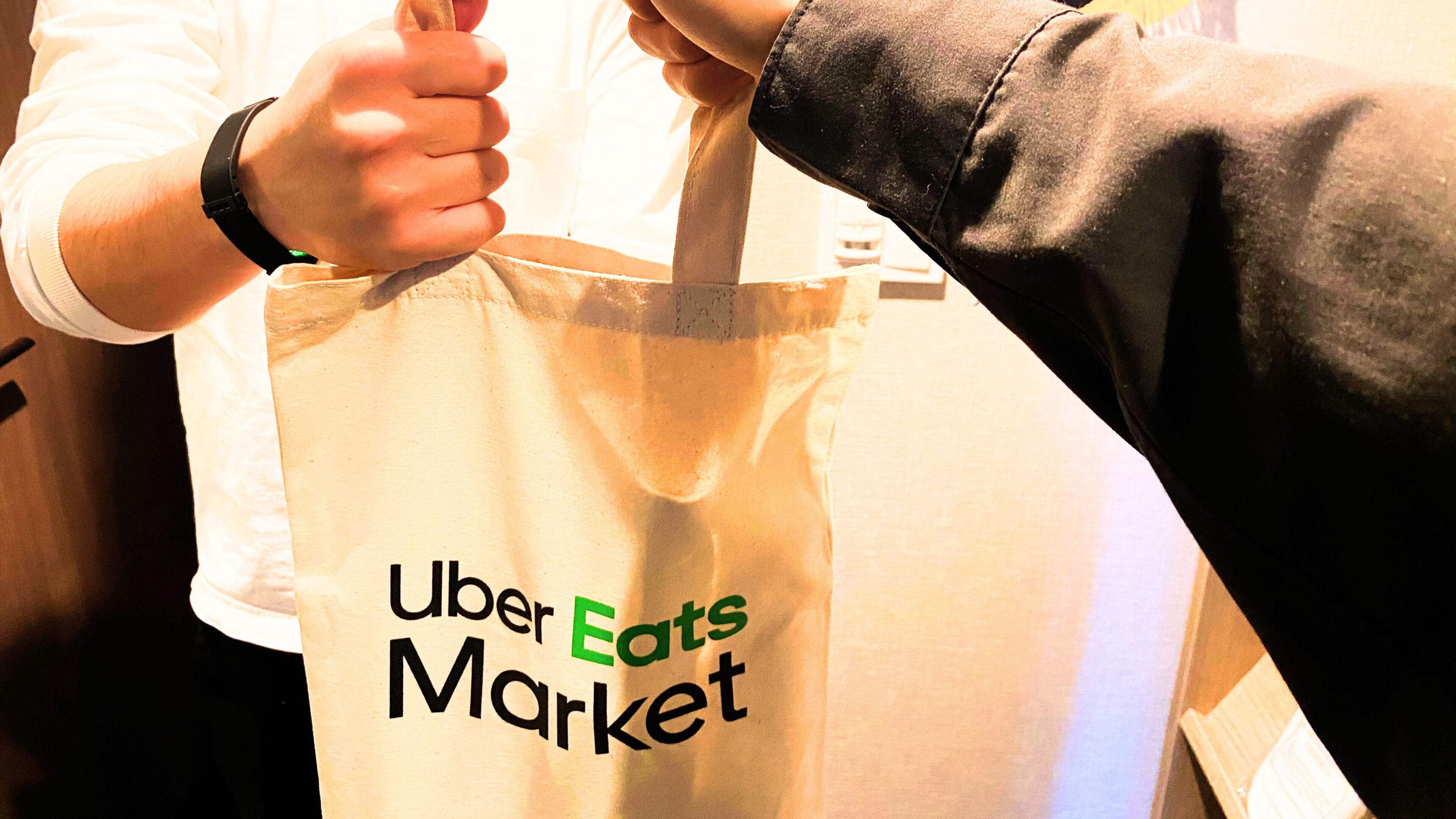 Una persona sosteniendo una bolsa de papel blanca con la frase 'Uber Eats Market' impresa.
