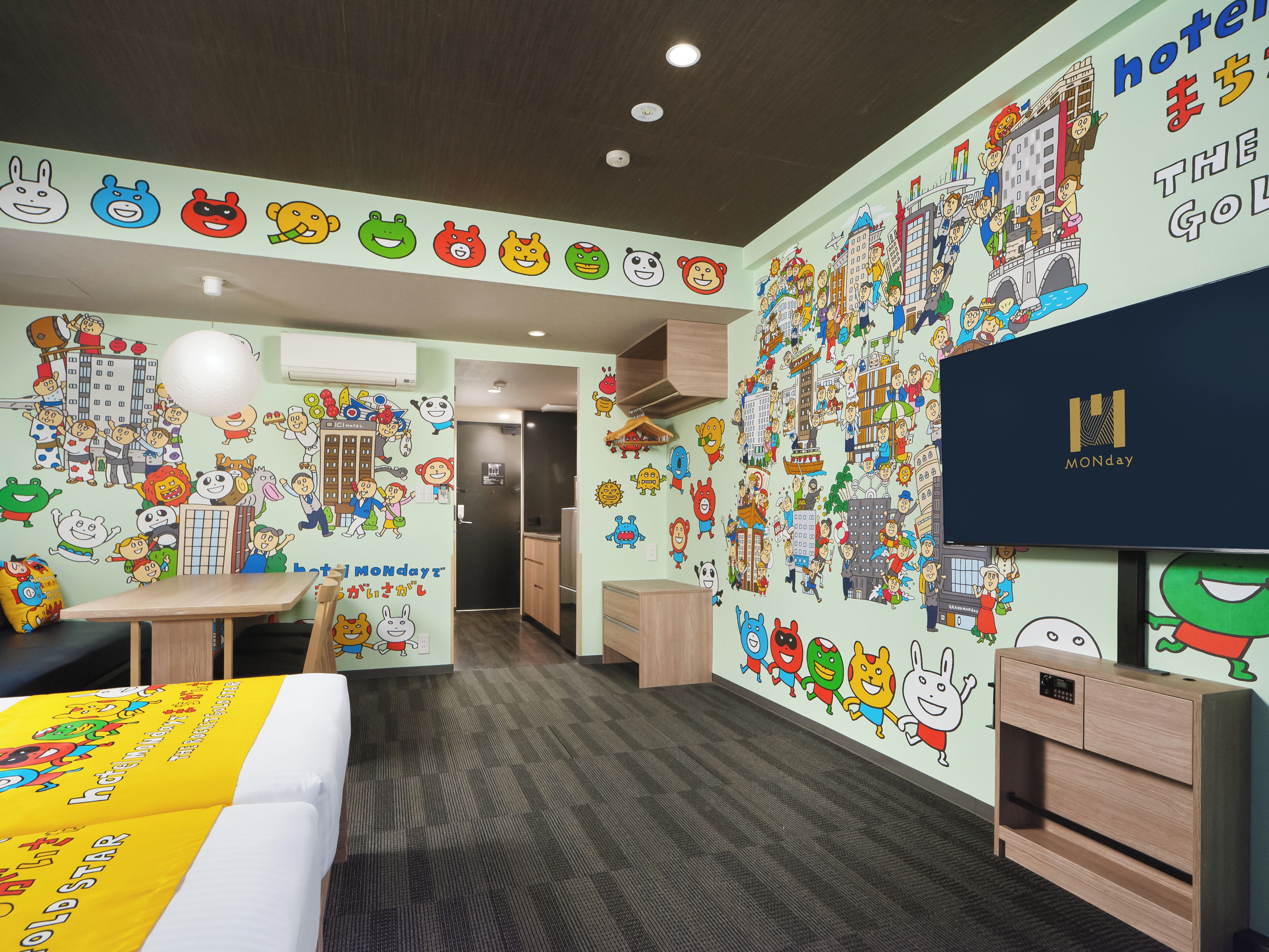A hotel room with a bed, a desk, a TV, and walls decorated with cartoon characters.