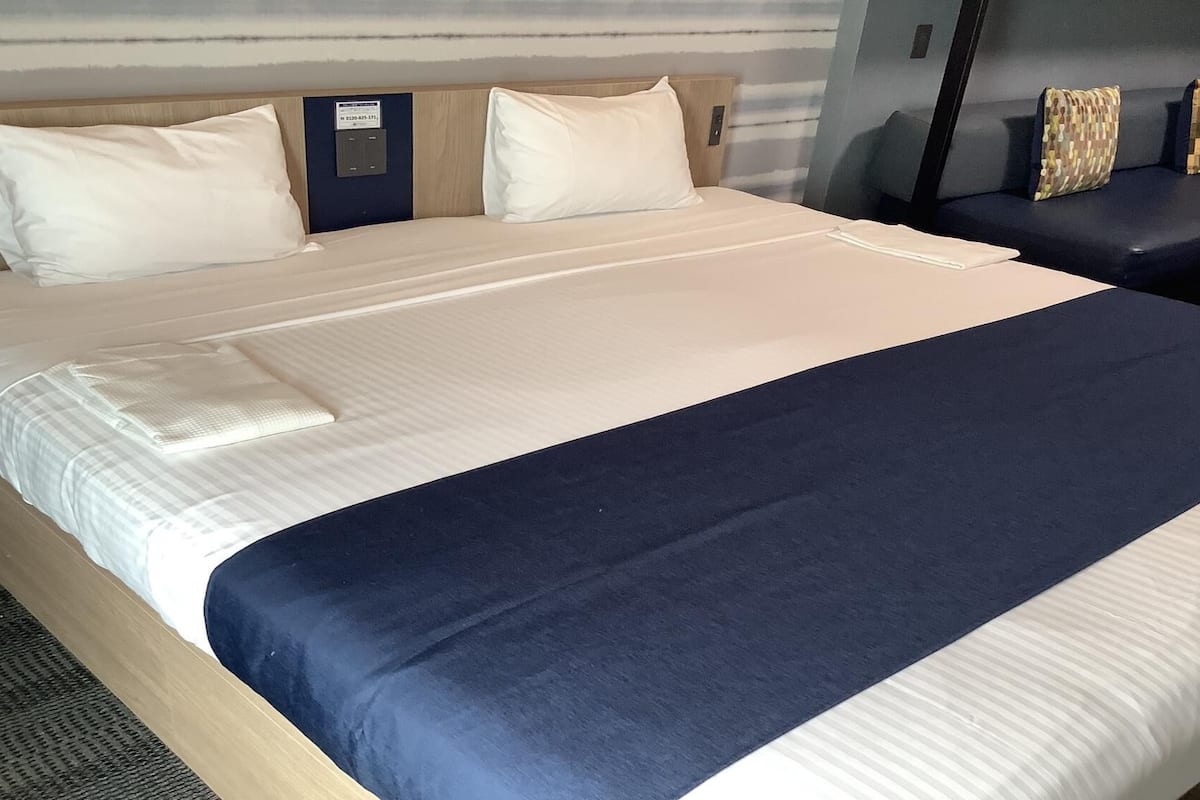 Quarto de hotel com uma cama grande, uma mesinha de cabeceira e um criado-mudo.