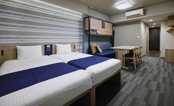 Et hotelværelse med to senge, køjeseng, et skrivebord og en stol.