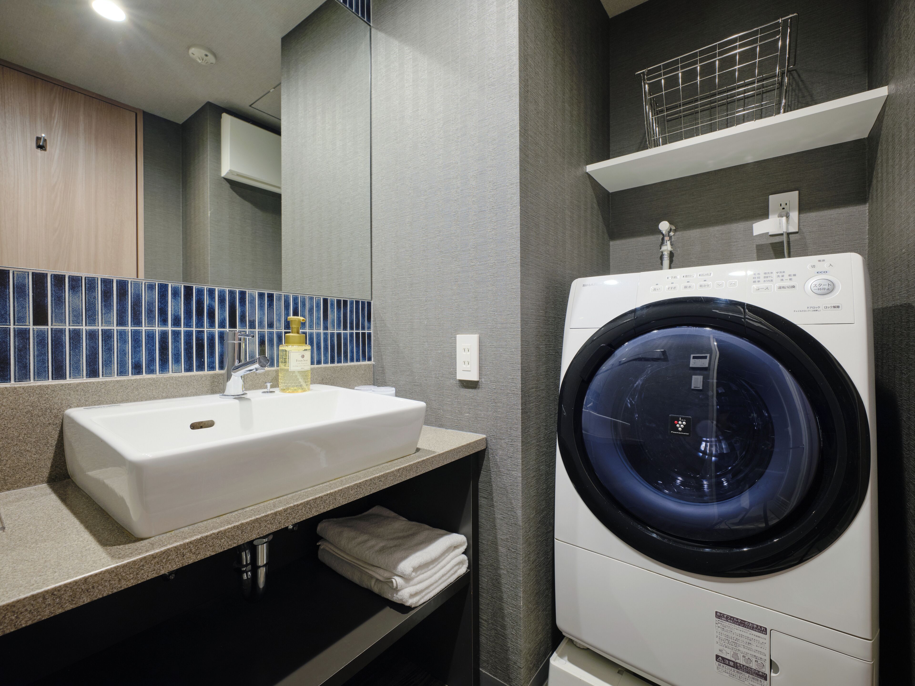 A modern bathroom with a white sink, a mirror, a blue-tiled backsplash, and a front-loading washing machine.
