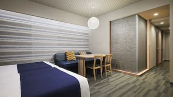 A hotel room with a large bed, a sofa, a small table, and a chair. There is a sliding door and a carpeted floor.