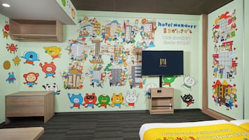 A hotel room with a large wall mural, a flat-screen TV, a wooden desk, and a bed with a cartoon-themed bedspread.
