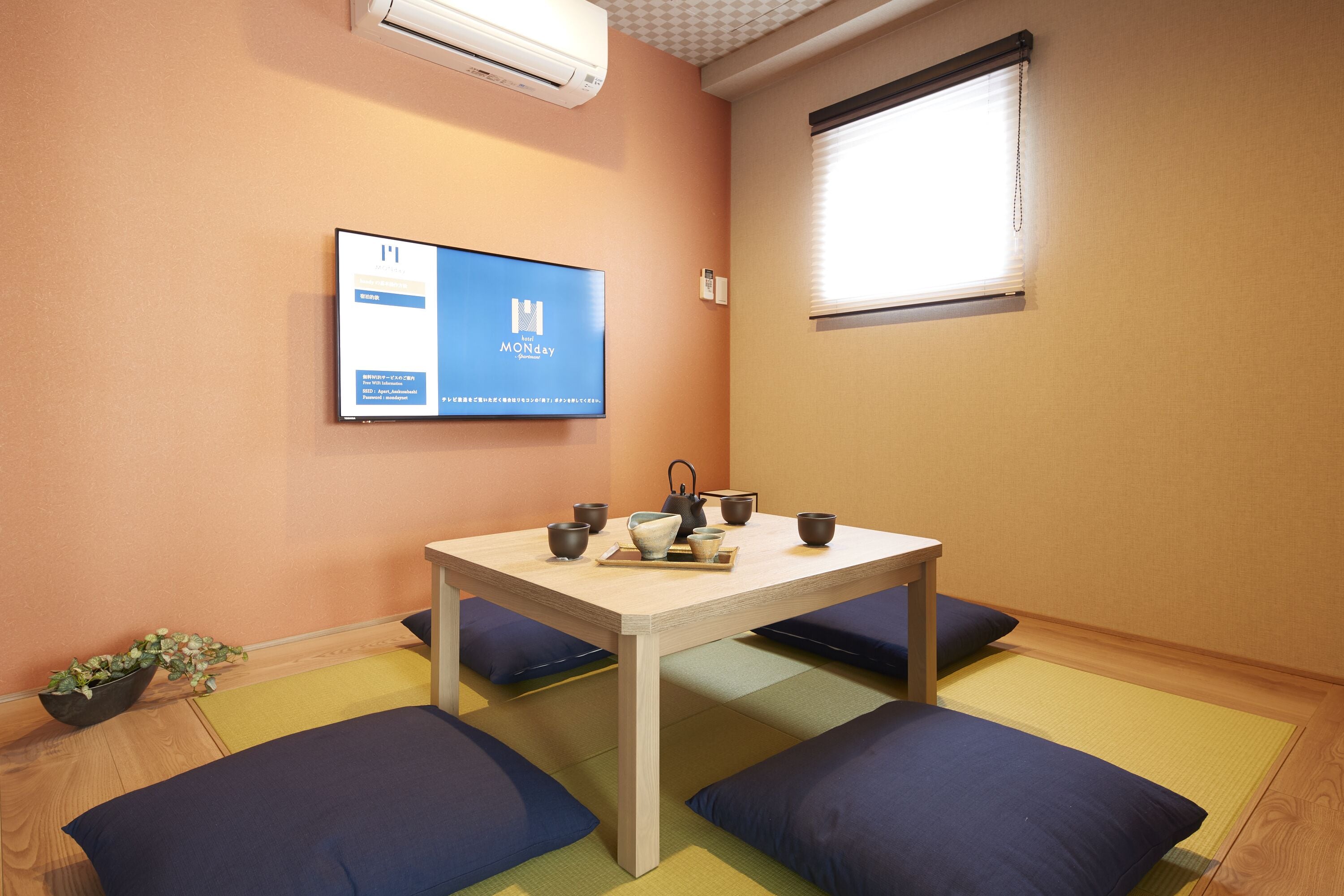 A room with a wooden table, blue cushions, a television displaying a website, and a window with blinds.