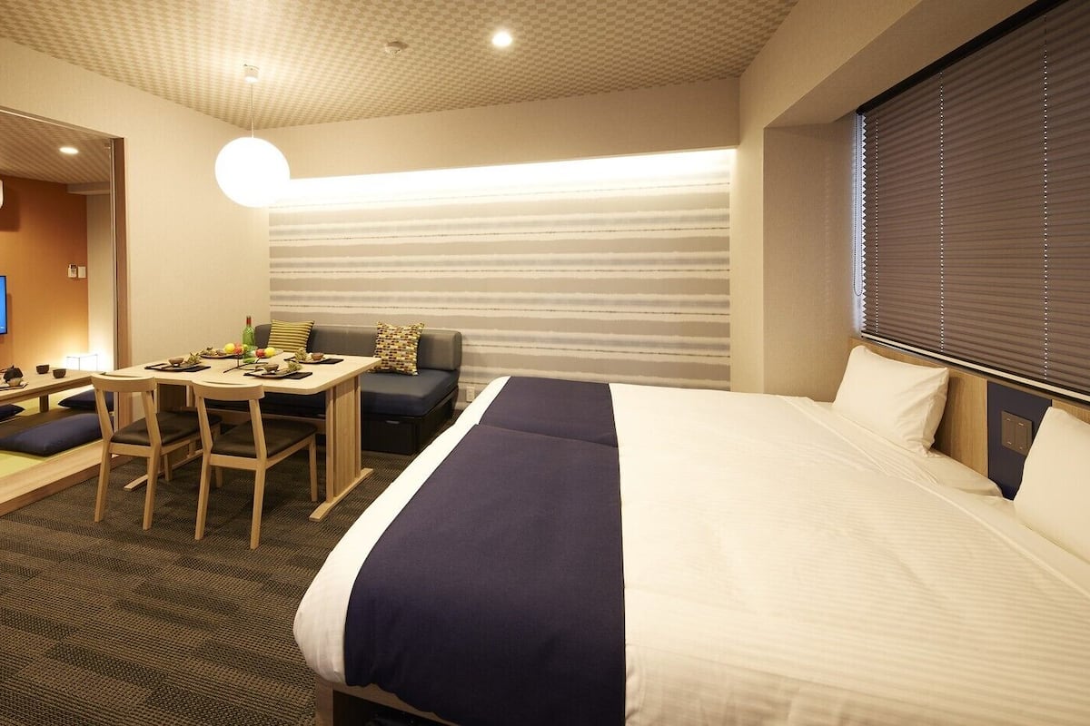 Quarto de hotel com cama, mesa de jantar, cadeiras, sofá e televisão.