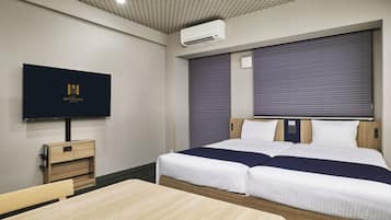 Una habitación de hotel con cama, televisión montada en la pared, mesita de noche y escritorio.
