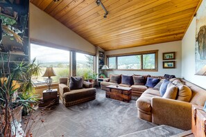 Relax in this serene living room with a sofa set, ottoman, and coffee table, surrounded by lush greenery and framed artwork.