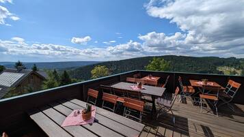 Eine Holzterrasse mit Tischen und Stühlen mit Blick auf eine bewaldete Landschaft.