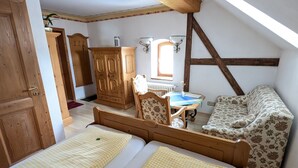 Un dormitorio acogedor en el ático con dos camas individuales, un armario de madera, un sofá floral y una mesita con un florero.
