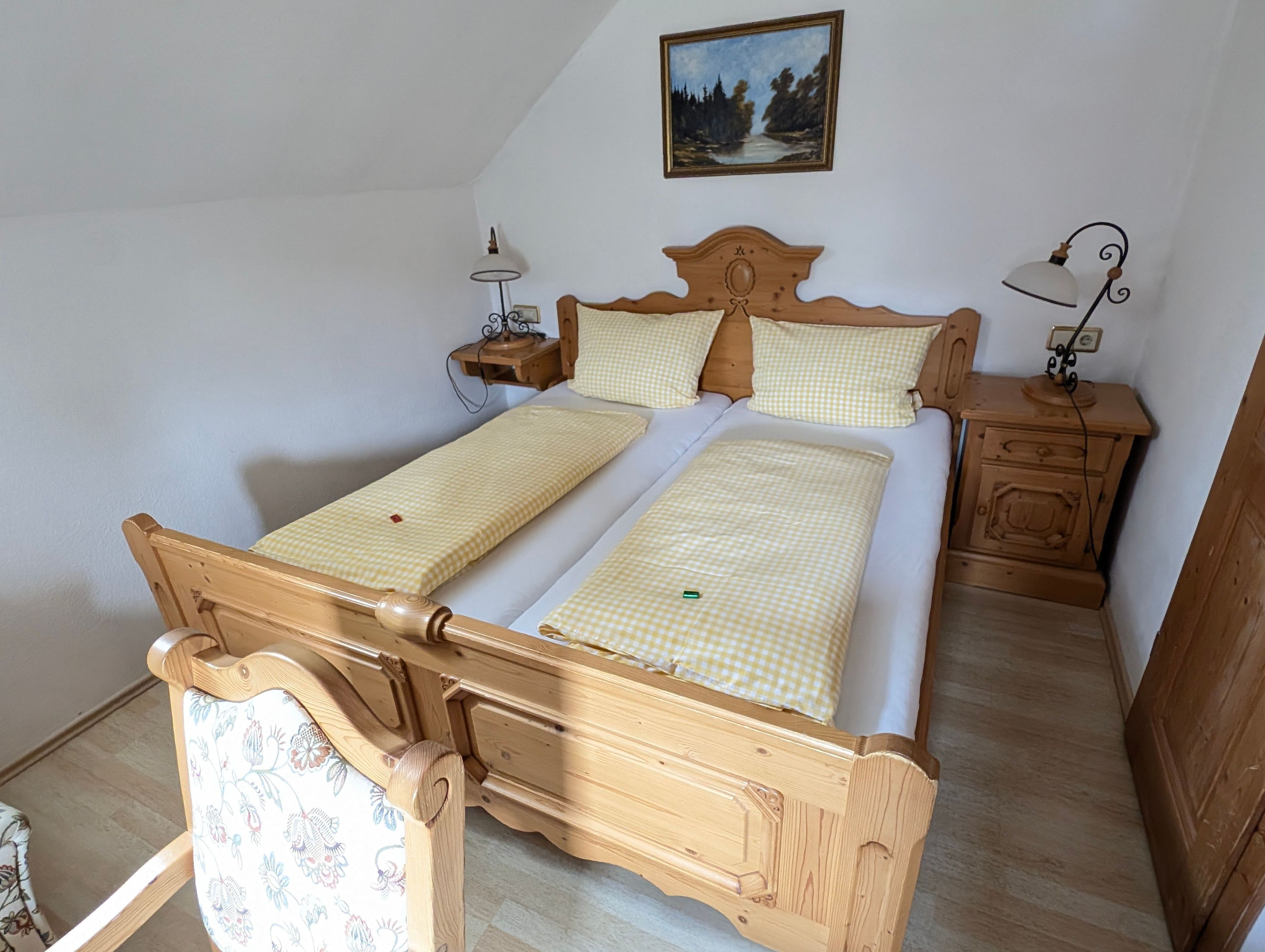 A wooden bed with checkered bedding, two bedside tables with lamps, and a painting on the wall.
