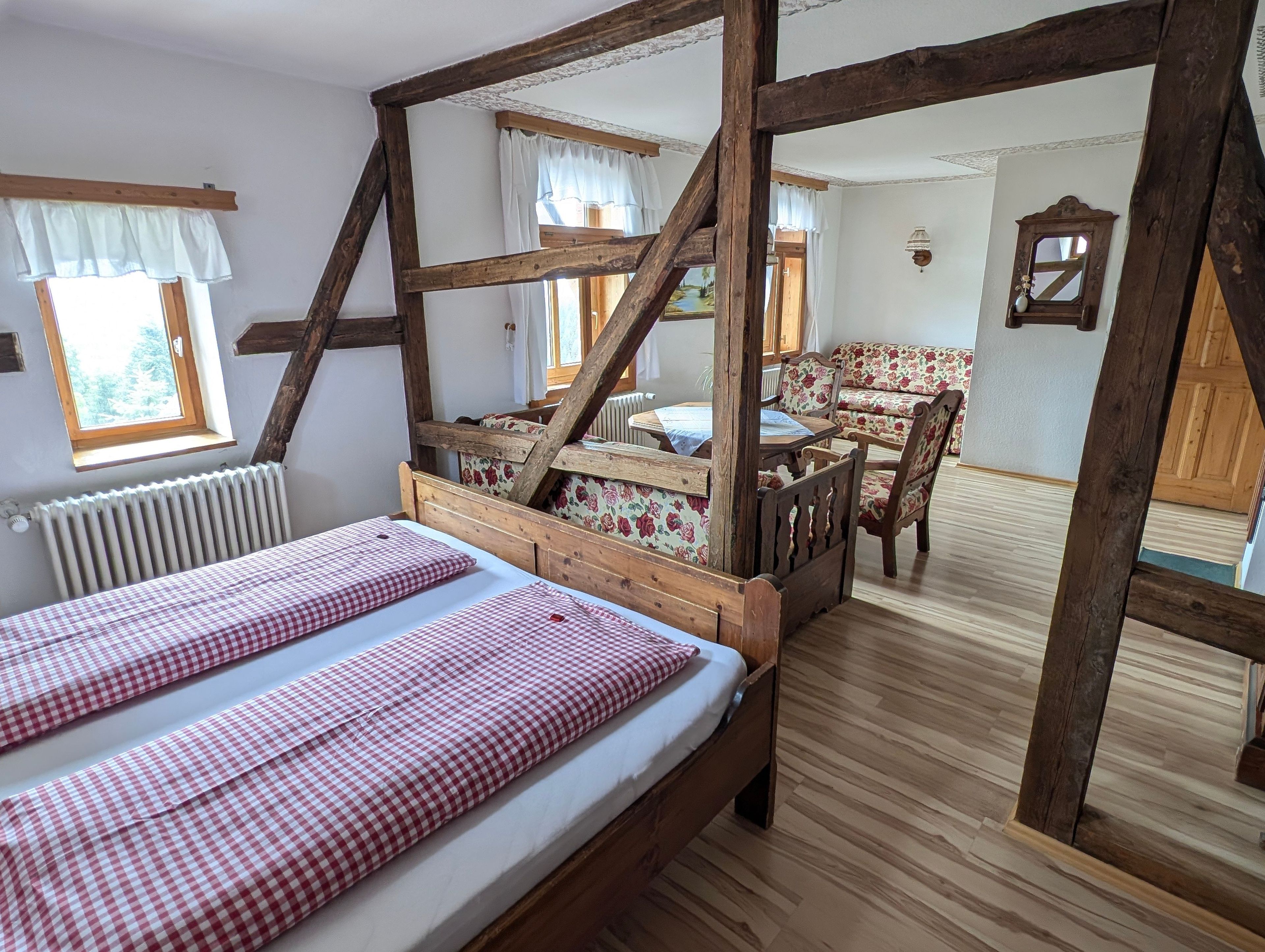 Une chambre dotée d’un lit à baldaquin, d’une table en bois avec des chaises, et offrant une vue sur une forêt par la fenêtre.
