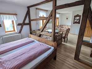 A room with a four-poster bed, a wooden table with chairs, and a view of a forest through a window.