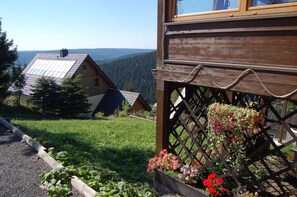 Une cabane en bois avec un toit en pente, une terrasse en bois et un jardin fleuri.