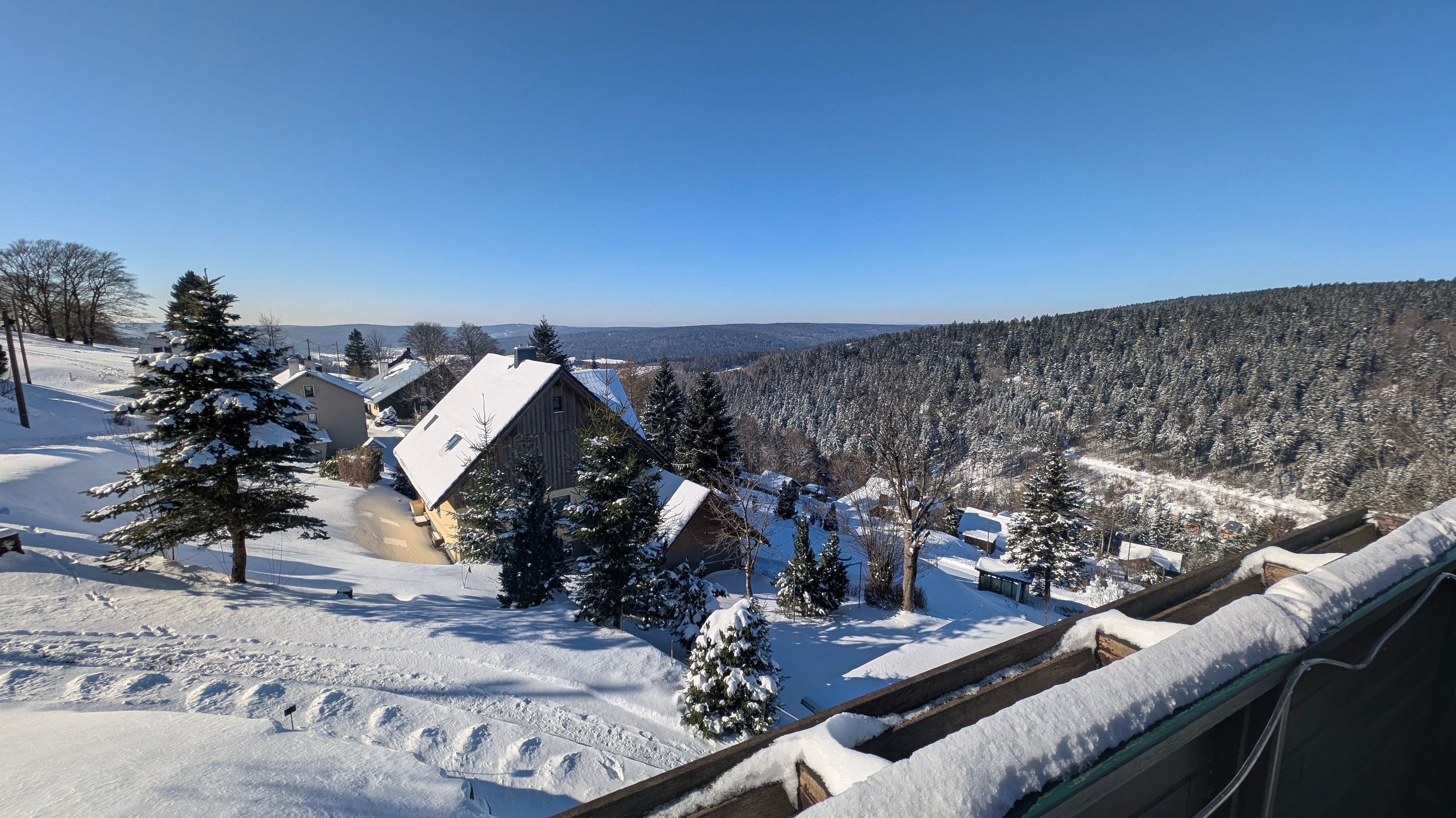 A snowy landscape with houses, trees, and a clear sky.