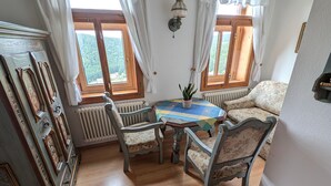Una habitación con suelo de madera, una mesa con sillas, un sofá, un radiador y una ventana con cortinas.