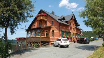 Ein traditionelles Backsteinhaus mit Balkon, davor ein geparktes Auto und ein Schild, das ein Restaurant anzeigt.