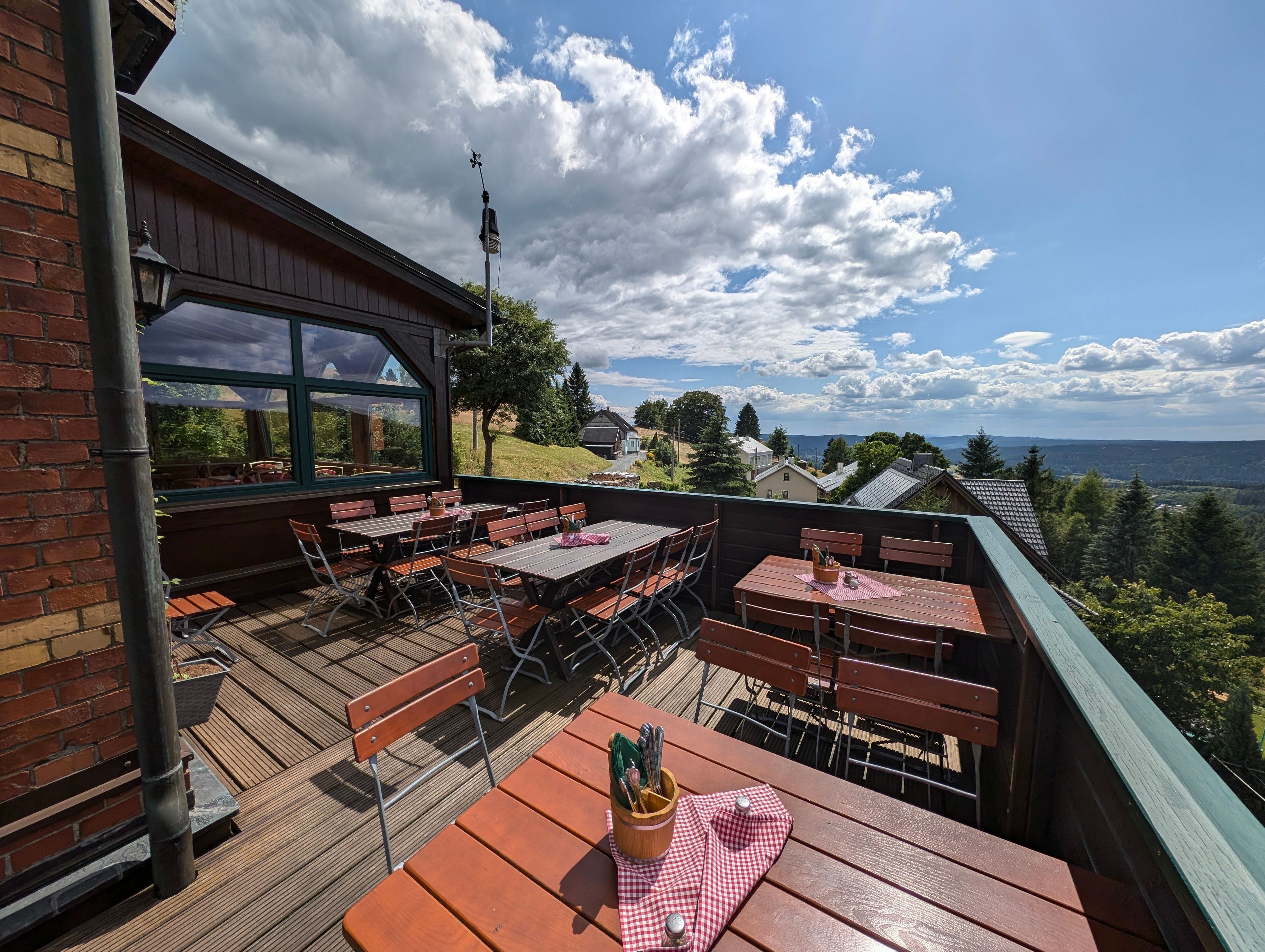 An outdoor seating area with tables and benches, a view of the landscape, and a building with a green roof.