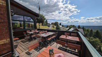 An outdoor seating area with tables and benches, a view of the landscape, and a building with a green roof.