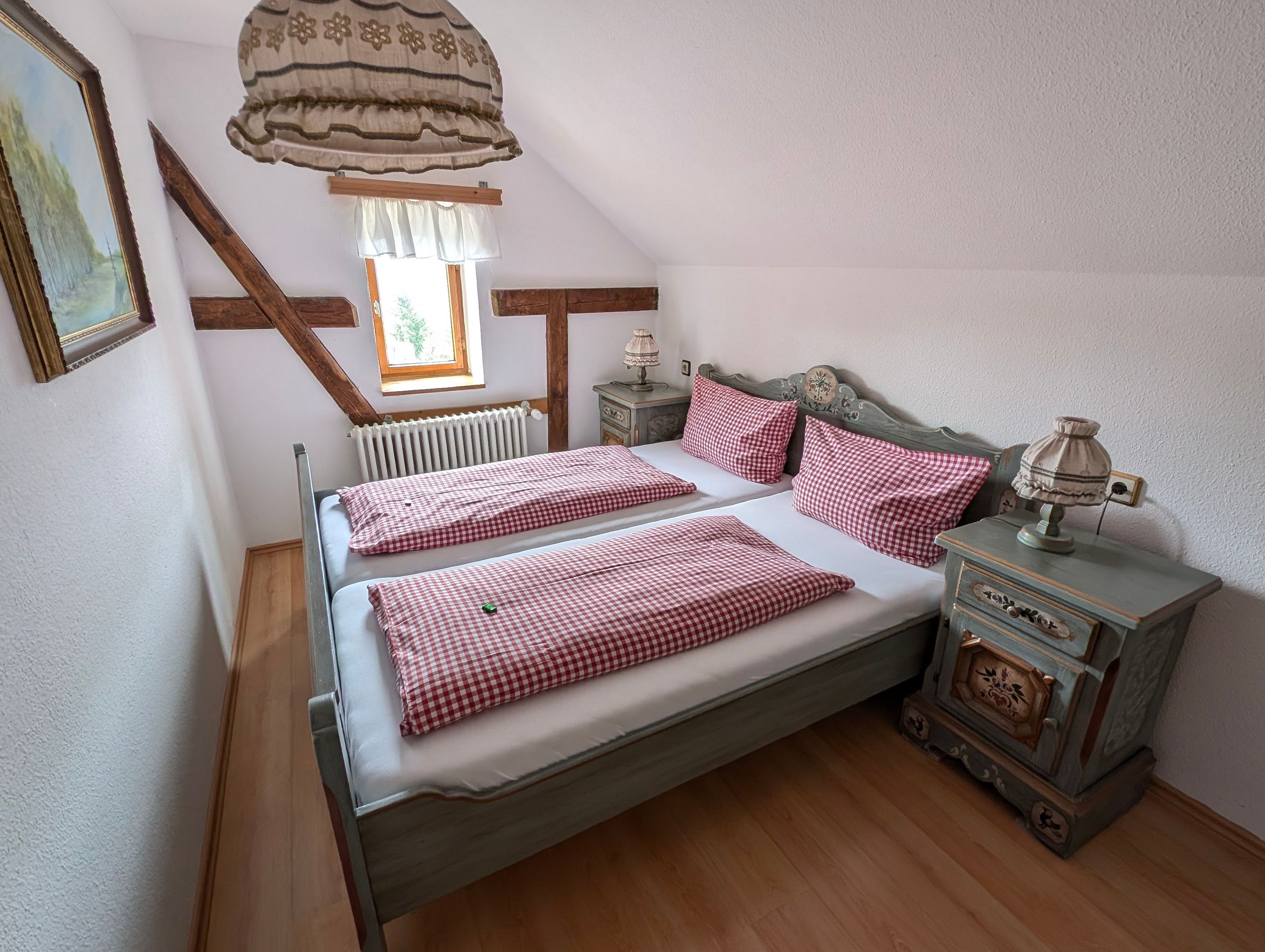 A bedroom with a bed, a nightstand, a lamp, and a window.