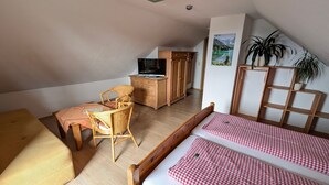 Une chambre mansardée chaleureuse, avec un lit en bois, une chaise en osier, une petite table et un téléviseur posé sur une commode en bois.
