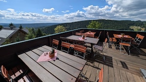 Une terrasse en bois, agrémentée de tables et de chaises, qui offre une vue sur un paysage boisé.