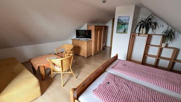 Ein gemütliches Schlafzimmer im Dachgeschoss mit einem hölzernen Bett, einem Korbstuhl, einem kleinen Tisch und einem Fernseher auf einer Holzkommode.