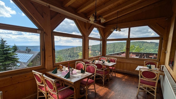 Un espace de restauration en bois, avec des tables et des chaises, de grandes fenêtres offrant une vue panoramique et un plafond en bois.