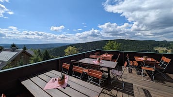 Eine Holzterrasse mit Tischen und Stühlen mit Blick auf eine bewaldete Landschaft.