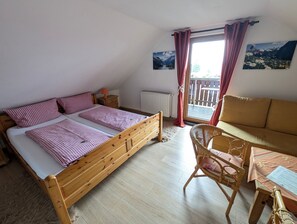 A bedroom with a wooden bed, a wicker chair, a small table, and a view of a balcony.