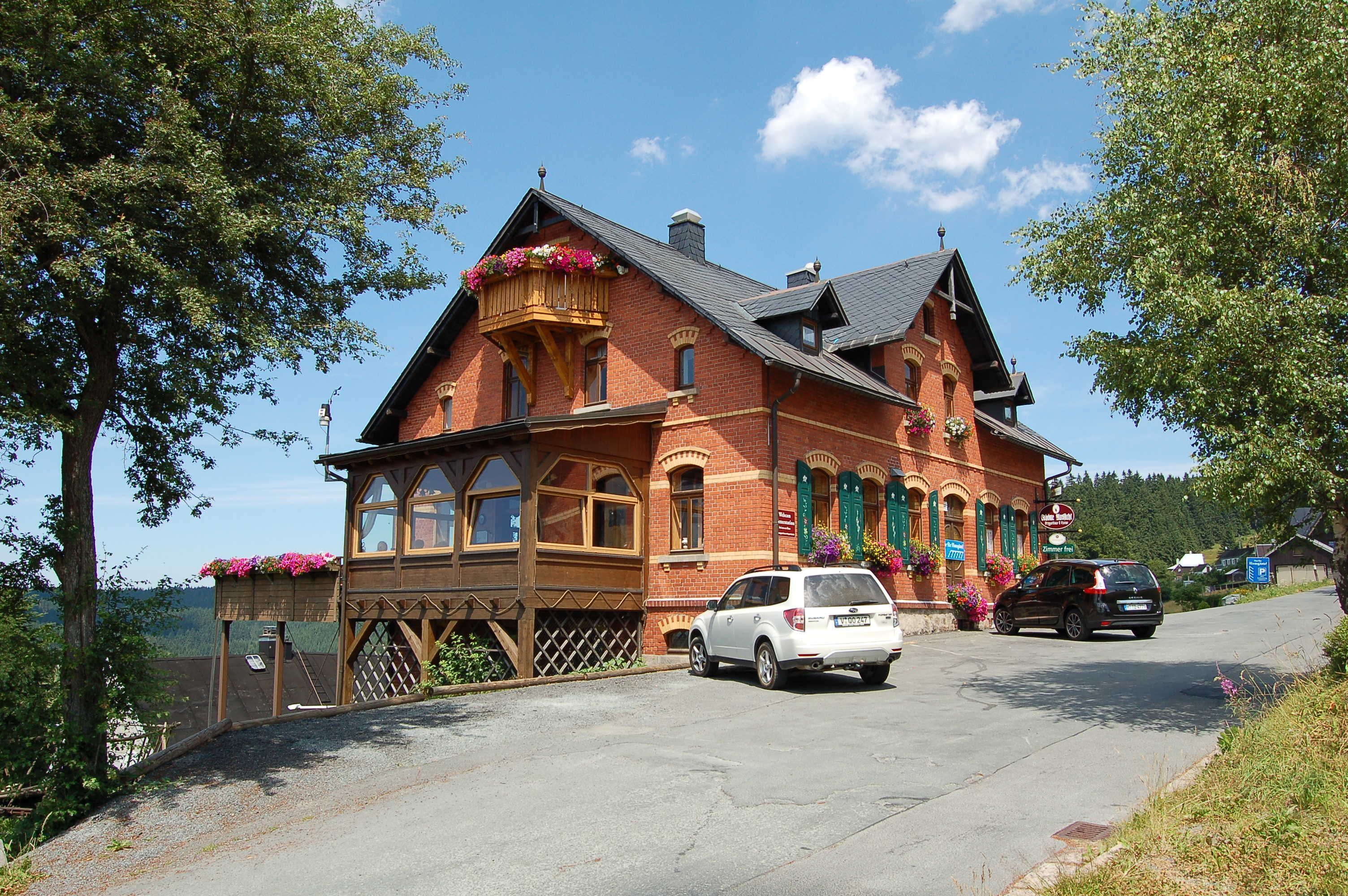 Un bâtiment traditionnel en briques, doté d’un balcon, avec une voiture garée devant et une enseigne indiquant qu’il s’agit d’un restaurant.