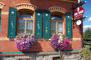 Un bâtiment en briques avec des volets verts, des jardinières et une enseigne indiquant qu’il s’agit d’un restaurant.