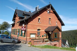 A red brick building with a balcony, a signboard, and a car parked in front.